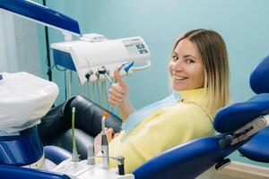 lindo menina paciente mostra a classe com dela mão enquanto sentado dentro a Dentistas cadeira foto