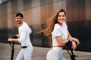 uma menina e uma cara estão caminhando em elétrico patinetes por aí a cidade, uma casal dentro amor em patinetes. foto