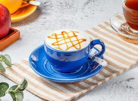 quente caramelo macchiato dentro azul copo em esteira com cinzento fundo café da manhã beber foto
