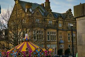 vintage construção com relógio torre atrás colorida carrossel dentro urbano configuração às crepúsculo dentro Harrogate, norte yorkshire, Reino Unido. foto