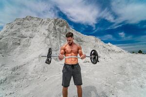 muscular sexy homem fazendo exercícios com barra ao ar livre. musculação e ao ar livre Esportes conceito. sessão de fotos dentro uma pedreira.