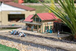 miniatura modelo do uma trem estação com minúsculo figuras e faixas, cercado de realista paisagismo. foto