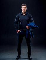 retrato do bonito jovem bem sucedido homem vestindo Sombrio camisa. homem segurando Sombrio azul jaqueta. Preto fundo. o negócio conceito. foto