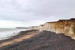 sereno de praia com giz falésias debaixo uma nublado céu, exibindo natural costeiro erosão e tranquilo marinha às Sete irmãs, Inglaterra. foto