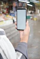 segurando inteligente telefone com esvaziar tela com borrado cafeteria rua fundo. foto