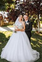 à moda, jovem noivo e lindo noiva dentro uma grandes branco vestir e uma grandes véu com uma ramalhete dentro seus mãos, abraçando dentro a parque dentro a outono natureza. Casamento retrato do recém-casados. foto