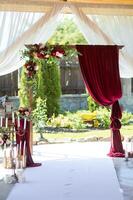 Casamento arco dentro restaurante. Sombrio vermelho flores e Borgonha cortinas. cerimônia decorações. foto