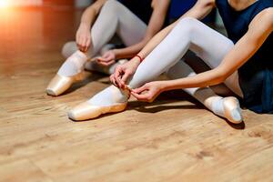 jovem balé dançarinos amarrar chinelos por aí seus tornozelos em a chão. meninas sentado em a chão e amarrar balé sapatos dentro balé estúdio. fechar acima. foto