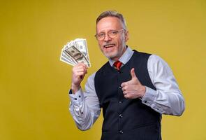 feliz idoso o negócio homem com ventilador do dólar contas isolado em amarelo fundo. Senior homem cara Ganhou a loteria. por sorte dia. humano emoções e facial expressões foto