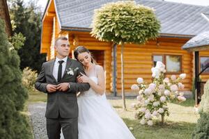 adorável e à moda recém-casados estão abraçando e sorridente contra a fundo do outono natureza dentro uma lindo jardim. a incrivelmente lindo jovem noiva inclinou-se contra a ombro do dela Amado noivo foto