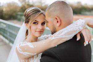 fofa e à moda recém-casados estão abraçando e sorridente contra a fundo do outono natureza dentro uma lindo jardim. a incrivelmente lindo jovem noiva Beijos dela amante foto