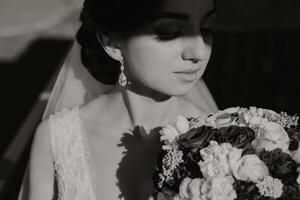 Preto e branco foto. a noiva é segurando uma ramalhete, posando com fechadas olhos. preparação para a celebração. lindo face. Casamento cerimônia. luz e sombra foto