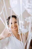 lindo morena noiva dentro uma branco vestir, manto, segurando branco gel bolas dentro dela mãos e desfrutando dela Casamento dia dentro dela sala. Casamento fotografia. foto