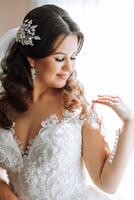 moda foto do uma lindo noiva com Sombrio cabelo dentro a elegante Casamento vestir e deslumbrante Maquiagem dentro a quarto em a manhã do a casamento. a noiva é preparando para a Casamento