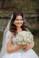 retrato. uma morena noiva dentro uma vestir e uma véu, com uma diadema, poses com uma ramalhete. prata joia. lindo Maquiagem e cabelo. outono casamento. celebração foto