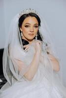 moda foto do uma lindo noiva com Sombrio cabelo dentro a elegante Casamento vestir e deslumbrante Maquiagem dentro a quarto em a manhã do a casamento. a noiva é preparando para a Casamento