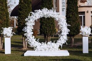 decoração às a casamento. uma volta arco decorado com branco flores e colunas contra uma árvore fundo. foto