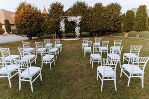 decoração às a casamento. muitos branco cadeiras e uma dourado arco decorado com branco flores foto