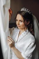 retrato do a incrivelmente lindo menina noiva dentro uma branco roupão dentro a quarto, a noiva poses dentro a manhã antes a Casamento cerimônia. foto