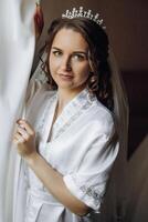 retrato do a incrivelmente lindo menina noiva dentro uma branco roupão dentro a quarto, a noiva poses dentro a manhã antes a Casamento cerimônia. foto