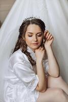 retrato do a incrivelmente lindo menina noiva dentro uma branco roupão dentro a quarto, a noiva poses dentro a manhã antes a Casamento cerimônia. foto