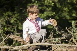 uma Garoto dentro a bordado camisa senta em a madeira. ucraniano ou bielorrusso criança foto