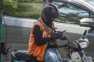 uma Comida Entrega pessoa ou vendedora Comida é levando ordens em dele Smartphone, Indonésia, 2 novembro 2023. foto