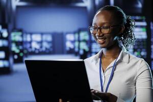 africano americano mulher entre servidor Fazenda linhas fornecendo em processamento Recursos para negócios mundialmente. admin fixação dados Centro montagens em rack encarregado com gerenciando maciço bases de dados foto