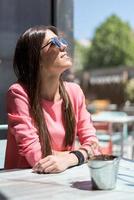 jovem feliz sentada no terraço de um restaurante com óculos escuros foto