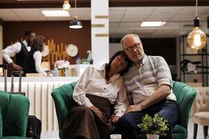 Exausta lindo idosos casal dormir em confortável sofás dentro luxuoso hotel salão. esperando para check-in, aposentado Senior Viajantes levando uma sesta dentro salão área depois de uma grandes voo. foto