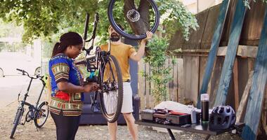 Atlético Preto mulher meticulosamente corrigindo danos em bicicleta cadeia com especializado ferramenta e jovem homem carregando fixo pneu determinado interracial casal recolocando e protegendo bicicleta rodas. foto