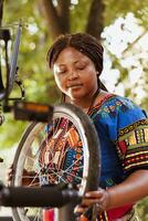 fechar-se do fêmea africano americano ciclista carregando bicicleta roda para anual verão manutenção ao ar livre. saudável amante de esportes Preto mulher fixação e mudando borracha em bicicleta pneu dentro casa quintal. foto