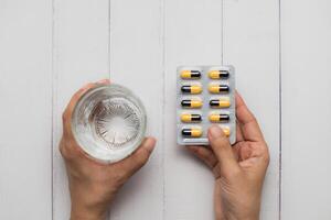 cuidados de saúde conceito com mão segurando água e pílulas em branco de madeira mesa foto
