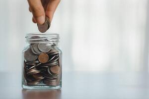 mão colocando moeda dentro vidro jarra para Salve  dinheiro para preparar dentro a futuro. foto
