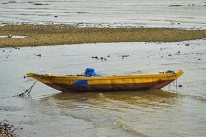 uma amarelo de madeira pescaria barco em a de praia foto
