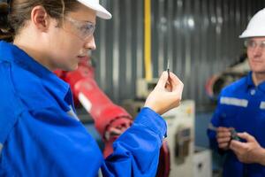 engenheiros e técnicos trabalhando juntos dentro uma robótico braço fábrica. Verifica a eletrônico poupar partes e elétrico sistema do a robótico braço. foto