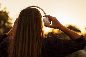 jovem mulher dentro fones de ouvido ouvindo para música às pôr do sol foto