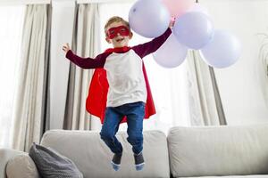 Garoto dentro Super heroi traje com balões pulando em sofá foto