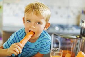 Garoto desfrutando cenoura dentro cozinha foto