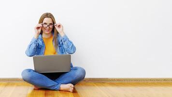 mulher sentado de pernas cruzadas em de madeira chão segurando computador portátil foto