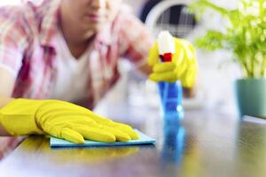 dona de casa dentro amarelo luvas lenços poeira usando spray detergente e trapo foto