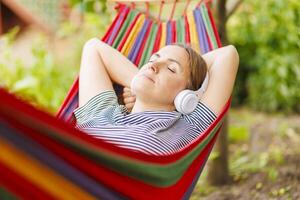 jovem mulher dentro fones de ouvido ouvindo para música enquanto em repouso dentro maca ao ar livre foto