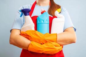 uma mulher dentro luvas e avental segurando limpeza produtos em azul fundo foto