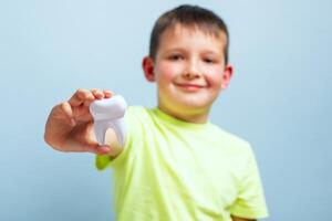 criança mostra grande branco brinquedo dente em uma azul fundo. carinhoso para dentes foto