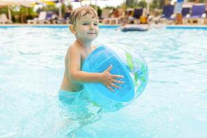criança nadar, mergulho, lazer e jogando inflável bola dentro piscina às período de férias foto