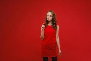 uma lindo menina dentro uma vermelho vestir em uma vermelho fundo detém uma morango dentro dela mãos e sorrisos foto