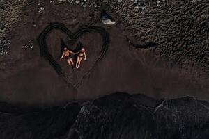 uma casal dentro amor mentiras em uma de praia do Preto vulcânico areia dentro uma pintado coração, tenerife, canário ilhas, Espanha foto