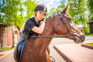 adorável jovem mulher vestindo capacete equitação dela Castanho cavalo foto