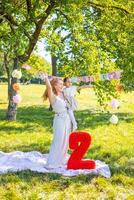 alegre mãe e filha tendo Diversão em criança aniversário em cobertor com papel decorações dentro a parque foto