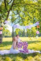 alegre mãe e filha tendo Diversão em criança aniversário em cobertor com papel decorações dentro a parque foto